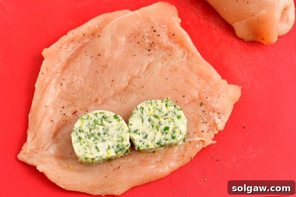 Two slices of chilled compound herb butter placed on a raw, flattened chicken breast cutlet, ready for rolling.