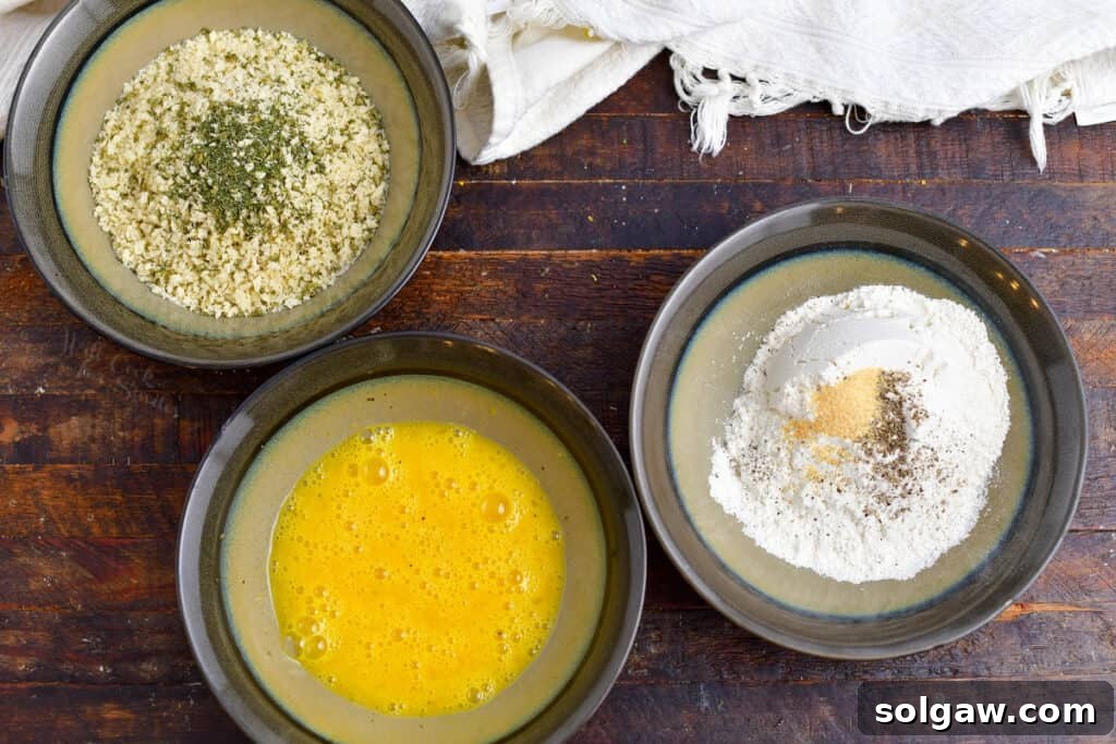 Three separate bowls containing seasoned flour, whisked egg yolks, and seasoned Panko breadcrumbs, ready for breading.