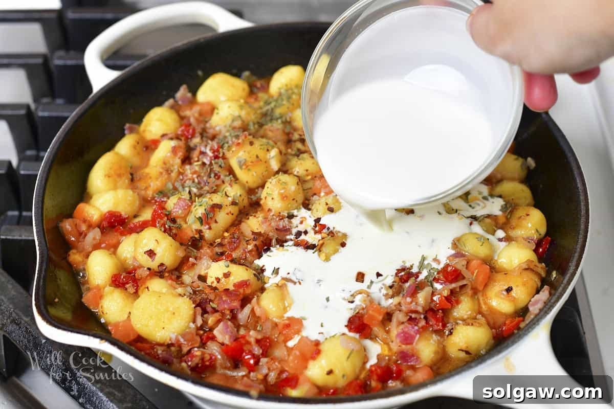 Adding rich heavy cream to the simmering gnocchi and sauce, making it luxuriously creamy.