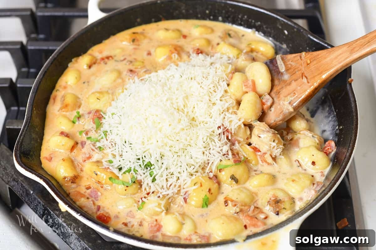 Adding a generous amount of freshly grated Parmesan cheese to the creamy gnocchi sauce in the pan.