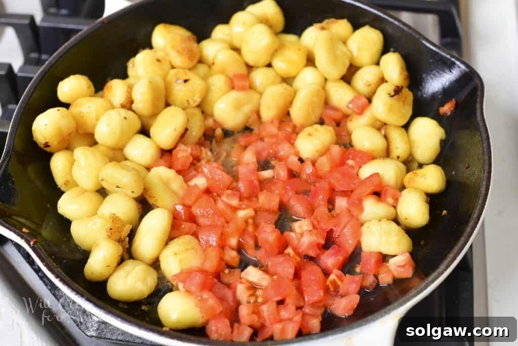 Adding fresh diced tomatoes to the pan with seared gnocchi, allowing them to soften slightly.