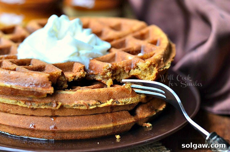 close up horizontal gingerbread waffles with whipped cream on top on a brown plate with a fork to the right