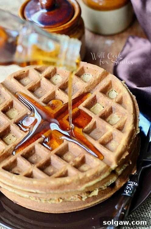 pouring syrup over ginger bread waffles with whipped cream on top on a brown plate with a fork to the right