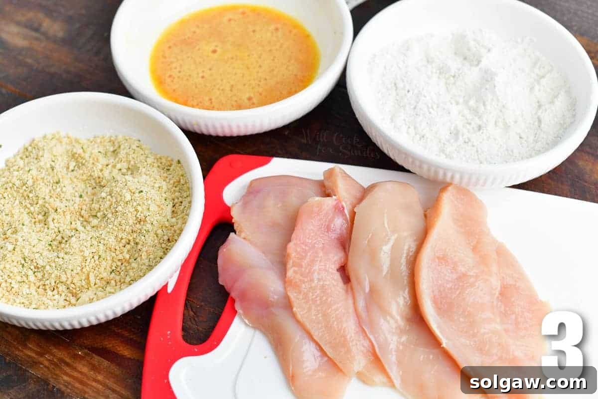 chicken breast cutlets and three bowls of flour, egg, and bread crumbs.