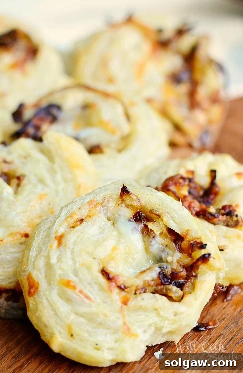 Golden Caramelized Onion Cheese Swirls 3 Caramelized Onion Cheesy Pinwheels on a wood cutting board, showcasing their layers and golden crust.