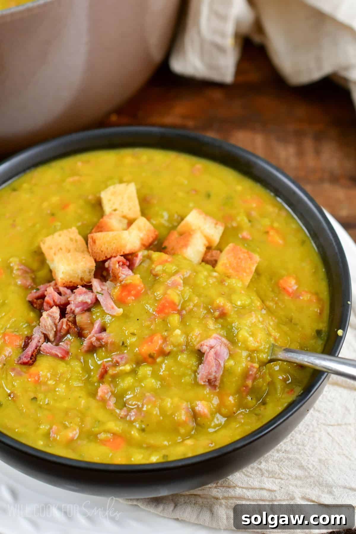 split pea soup in a bowl topped with croutons and ham with a spoon.