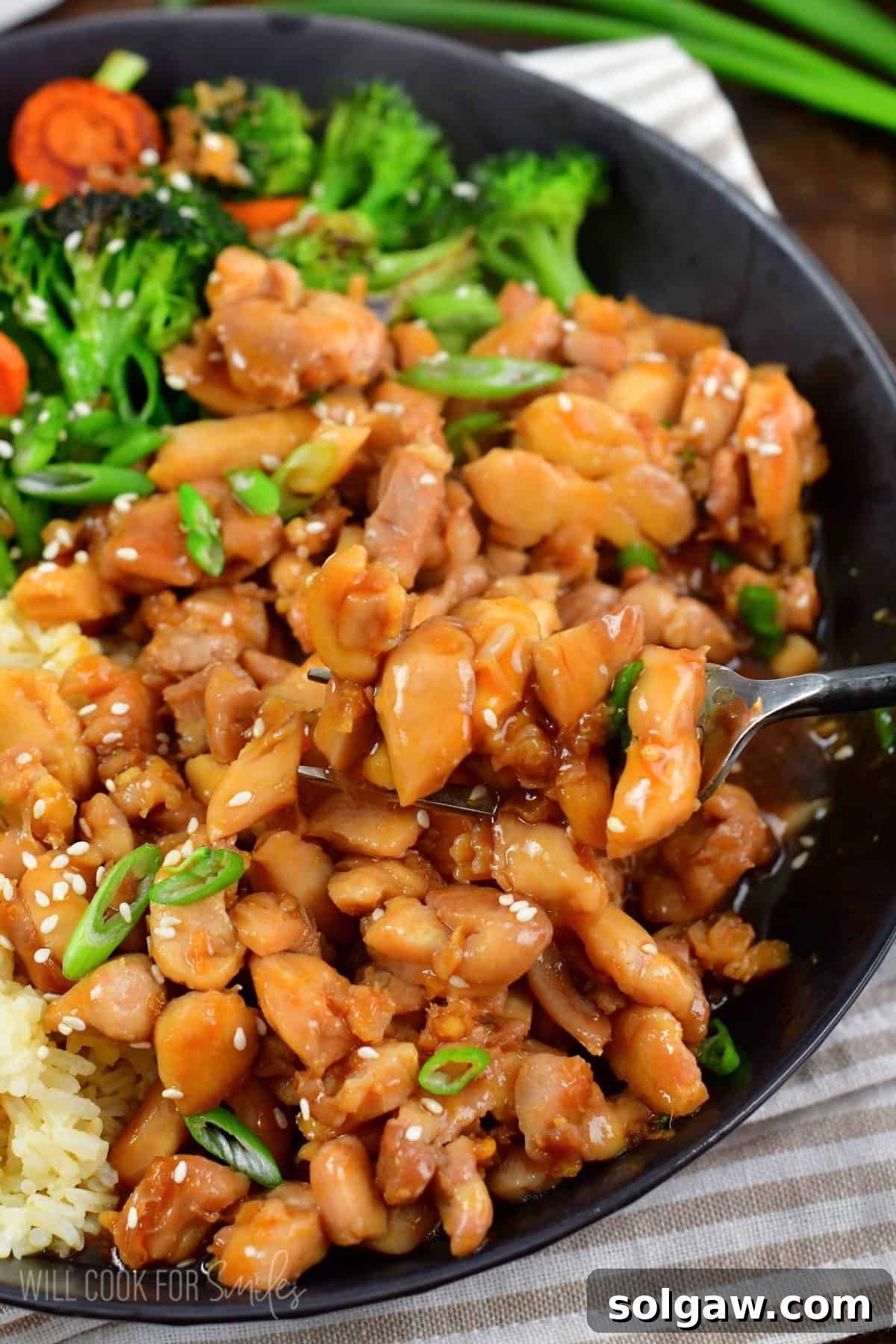 scooping some chicken teriyaki from a bowl with a fork.