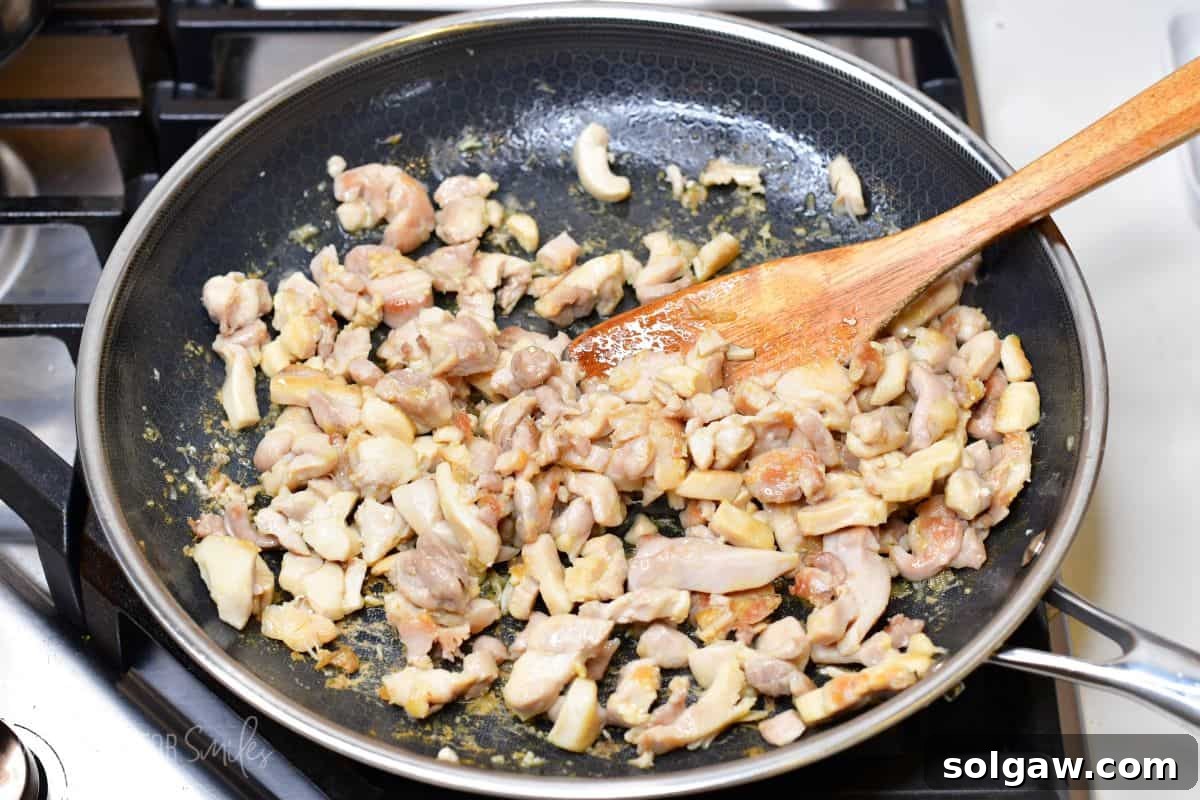 stirring browned chicken pieces in the pan.