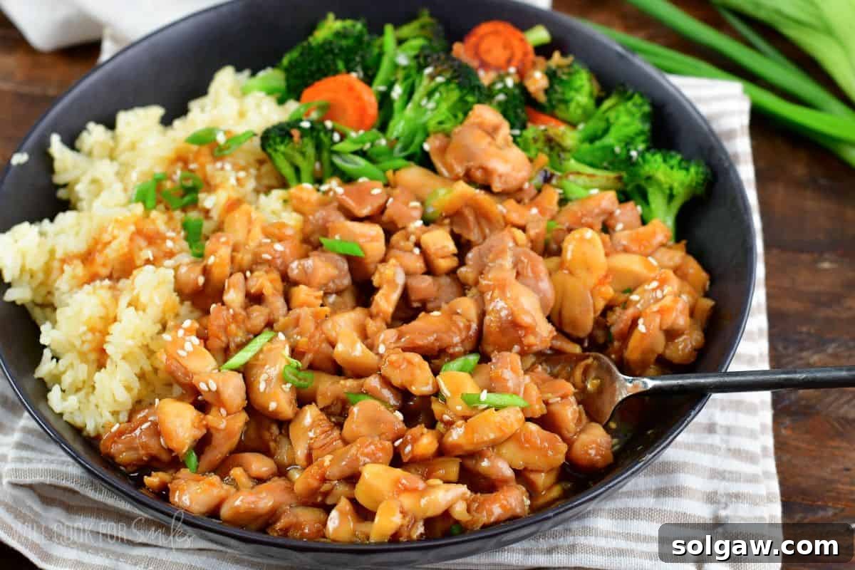 chicken teriyaki with rice, veggies, green onion and a fork in a black bowl.