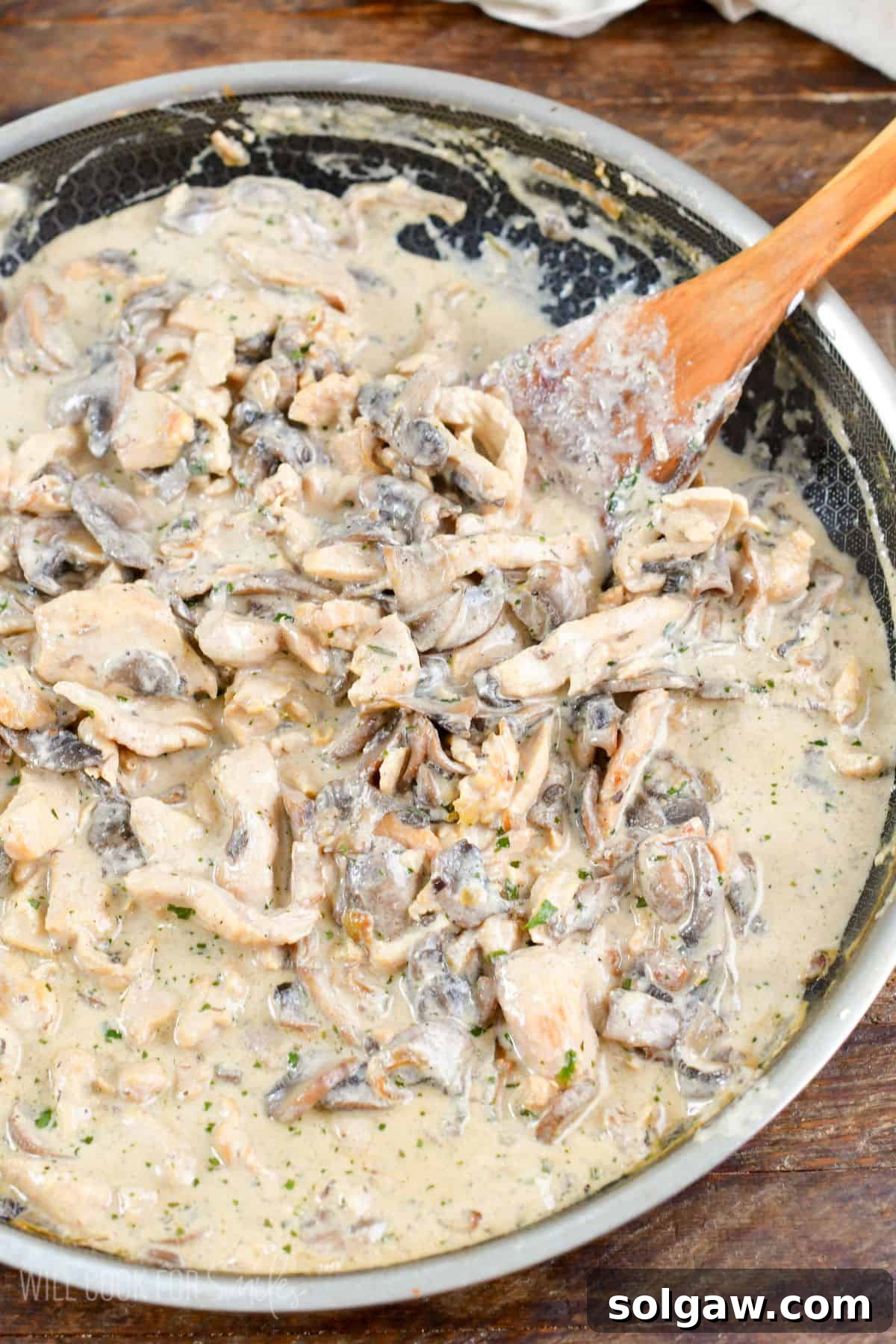 Luscious Weeknight Chicken Stroganoff 8 A top-down view of cooked chicken stroganoff in a large pan, showing the creamy sauce, tender chicken, and mushrooms, with a wooden spatula resting in the pan.