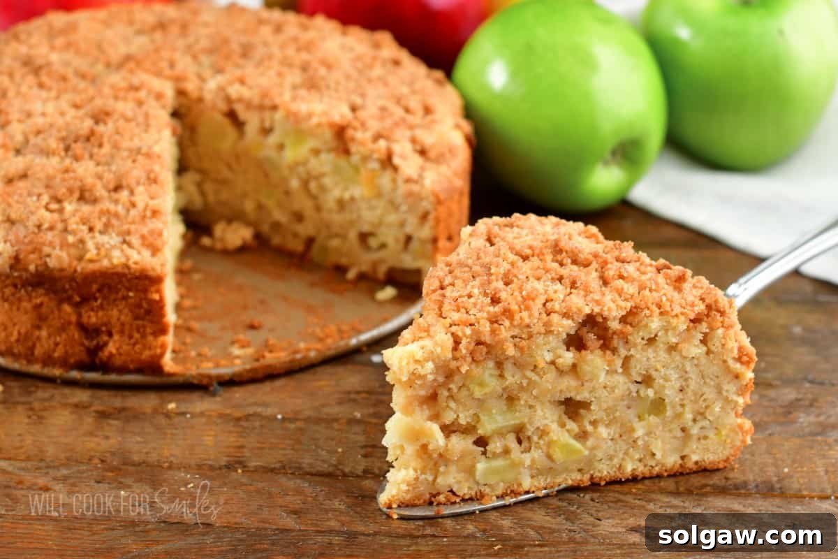 A side-by-side view of a whole, freshly baked Irish apple cake and a perfect slice next to it, showcasing the layers of cake, apple, and crumble.