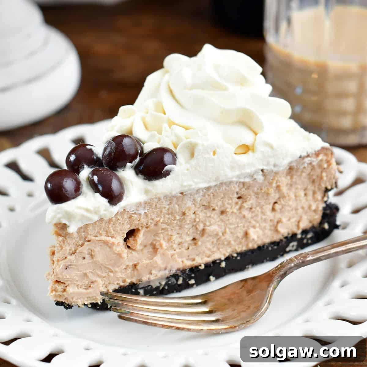 a slice of Baileys cheesecake on a white plate with a fork and some Irish cream in a glass.