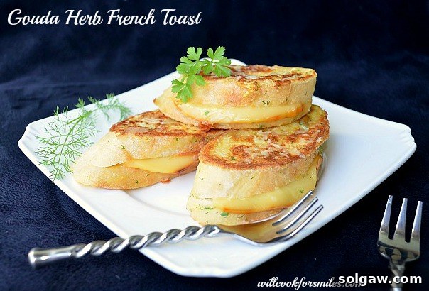 A slice of Gouda Herb Savory French Toast on a plate, with a fork cutting into it, revealing the melted cheese and fluffy interior.
