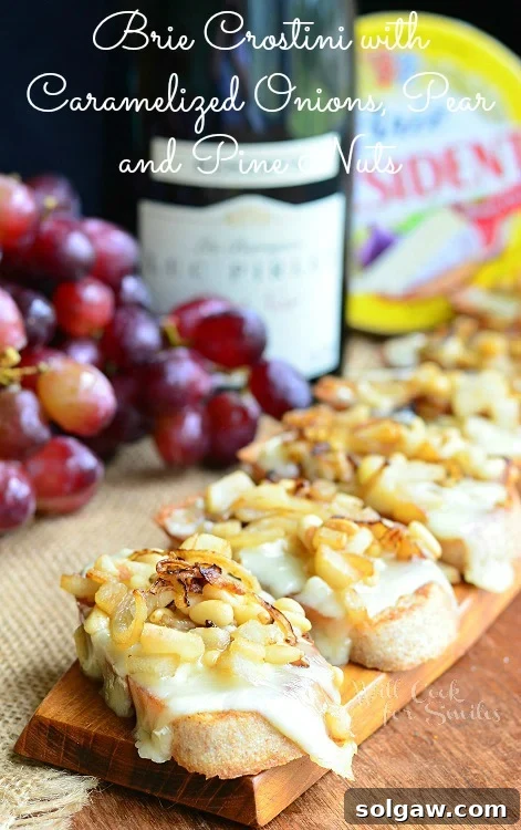Crispy Brie Crostini with Caramelized Onions, Pear, and Pine Nuts arranged beautifully on a wooden serving board