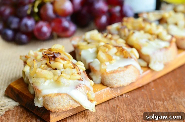 A serving tray laden with golden Brie Crostini, each generously topped with caramelized onions, diced pear, and toasted pine nuts, ready for serving