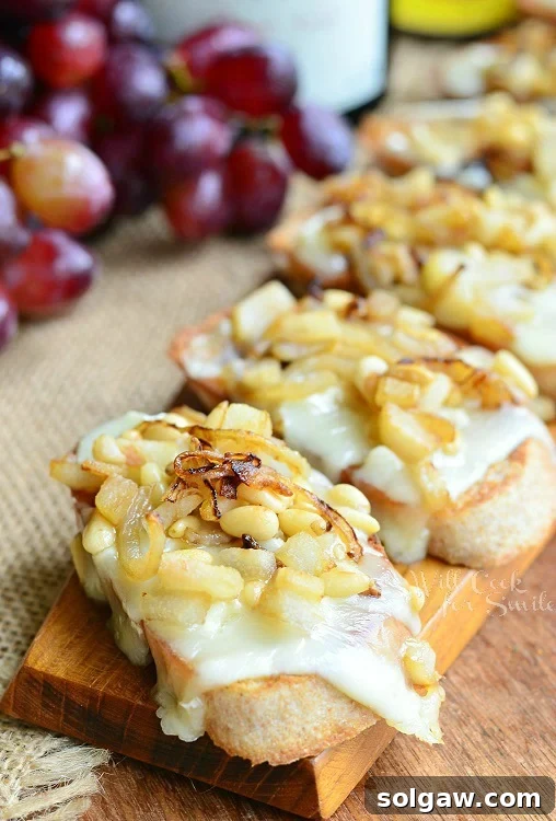 Close-up shot of a single Brie Crostini, showcasing the melted Brie, sweet caramelized onions, and tender diced pear, garnished with fresh herbs