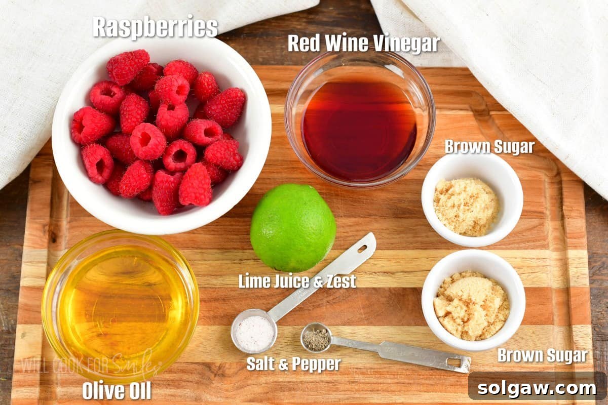 Sweet & Tangy Raspberry Drizzle 3 Labeled ingredients for making raspberry vinaigrette laid out on a cutting board, including fresh raspberries, lime, brown sugar, oil, and red wine vinegar.