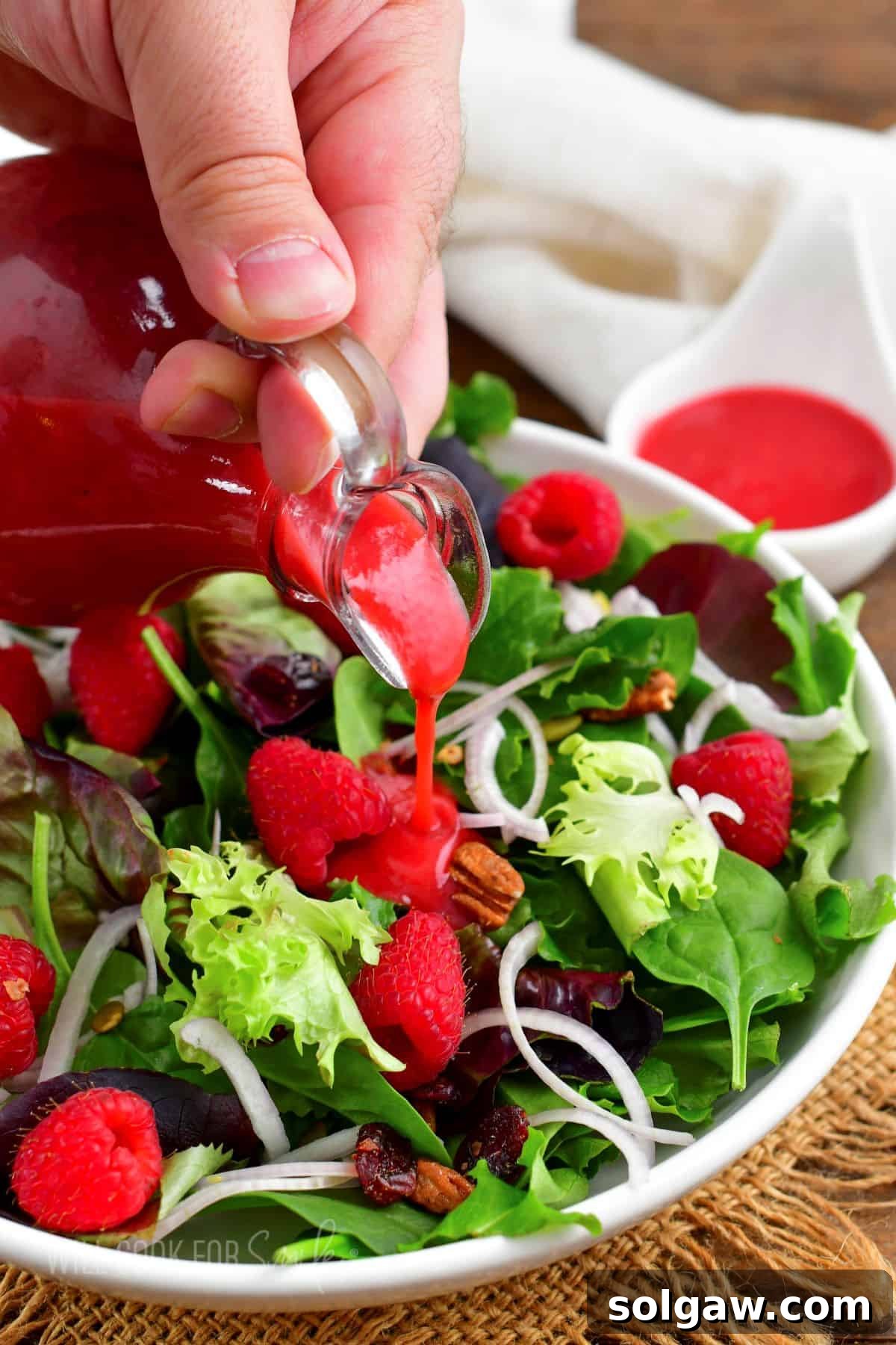 Sweet & Tangy Raspberry Drizzle 8 Pouring bright raspberry vinaigrette over a colorful spring salad filled with fresh berries, mixed greens, and crunchy nuts, ready to be enjoyed.