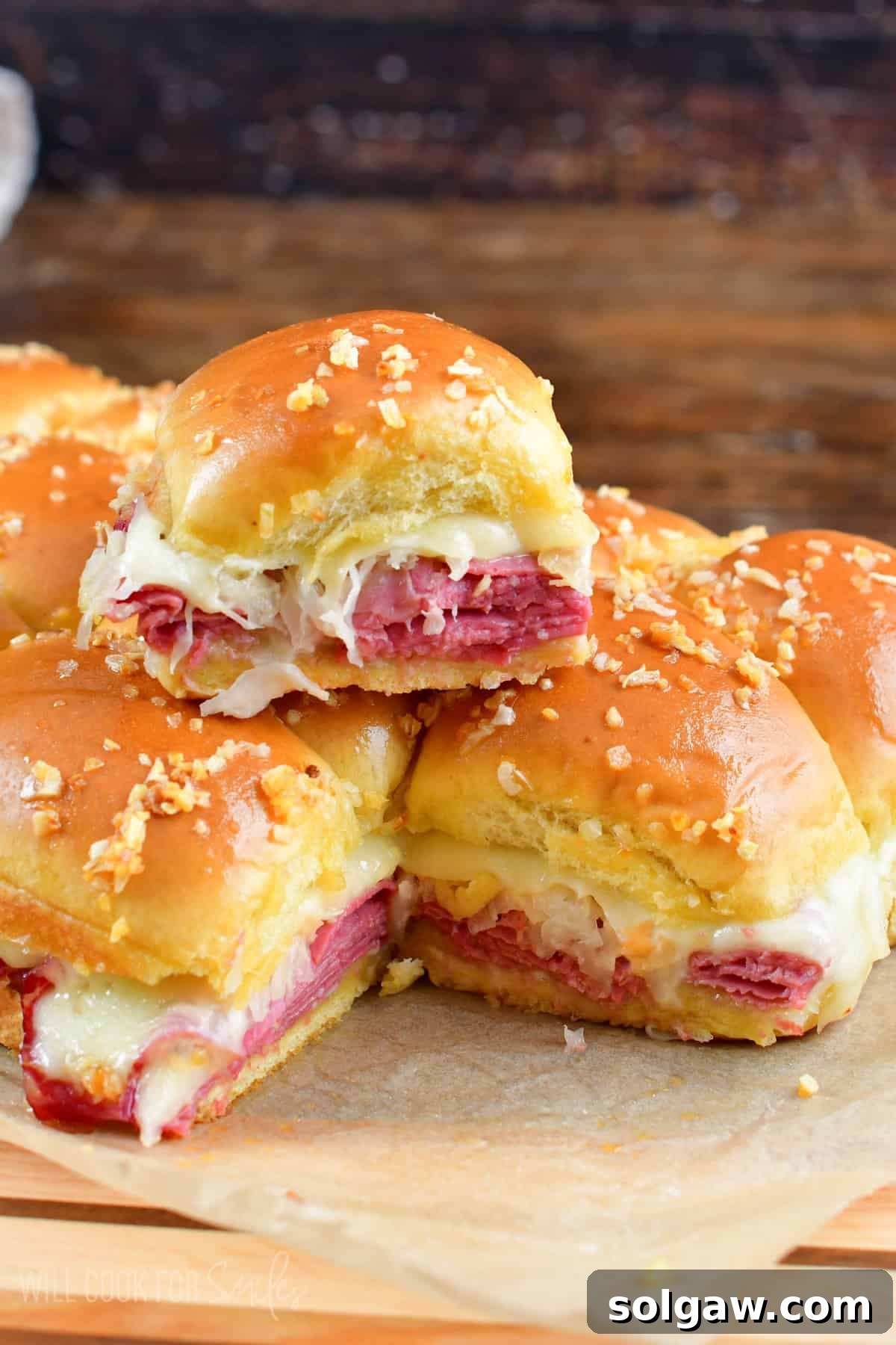Rueben sliders staked on parchment paper on a cutting board, garnished with fresh parsley.