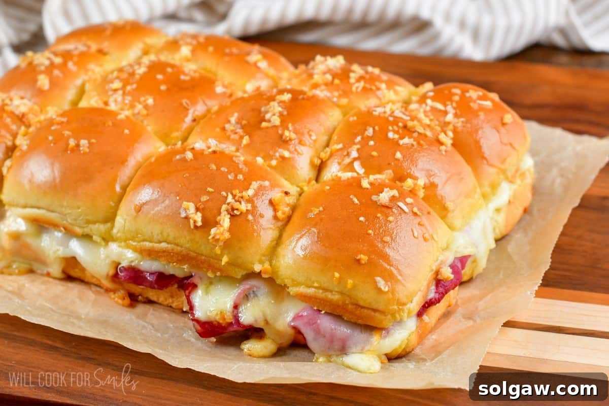 Baked Reuben sliders arranged on a piece of parchment paper on a wooden cutting board, ready to be served.