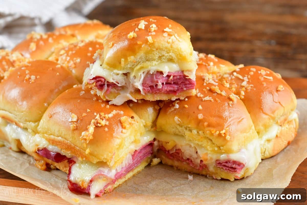 One Reuben slider stacked on top of the rest of the sliders on parchment paper, showing the melted cheese and golden bun.