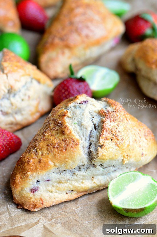 Sun-Kissed Strawberry Scones 2 Close-up of freshly baked Strawberry Key Lime Scones on butcher paper, garnished with fresh strawberries and whole key limes, highlighting their golden-brown exterior and juicy fruit