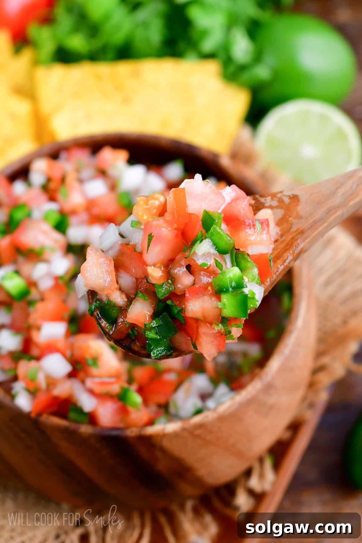 Scooping up fresh Pico de Gallo with a wooden spoon from a rustic bowl.