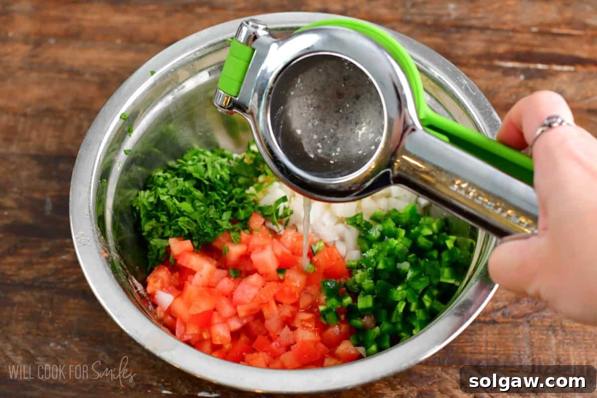 Squeezing a fresh lime directly into a bowl of chopped vegetables for Pico de Gallo, enhancing its vibrant flavors.