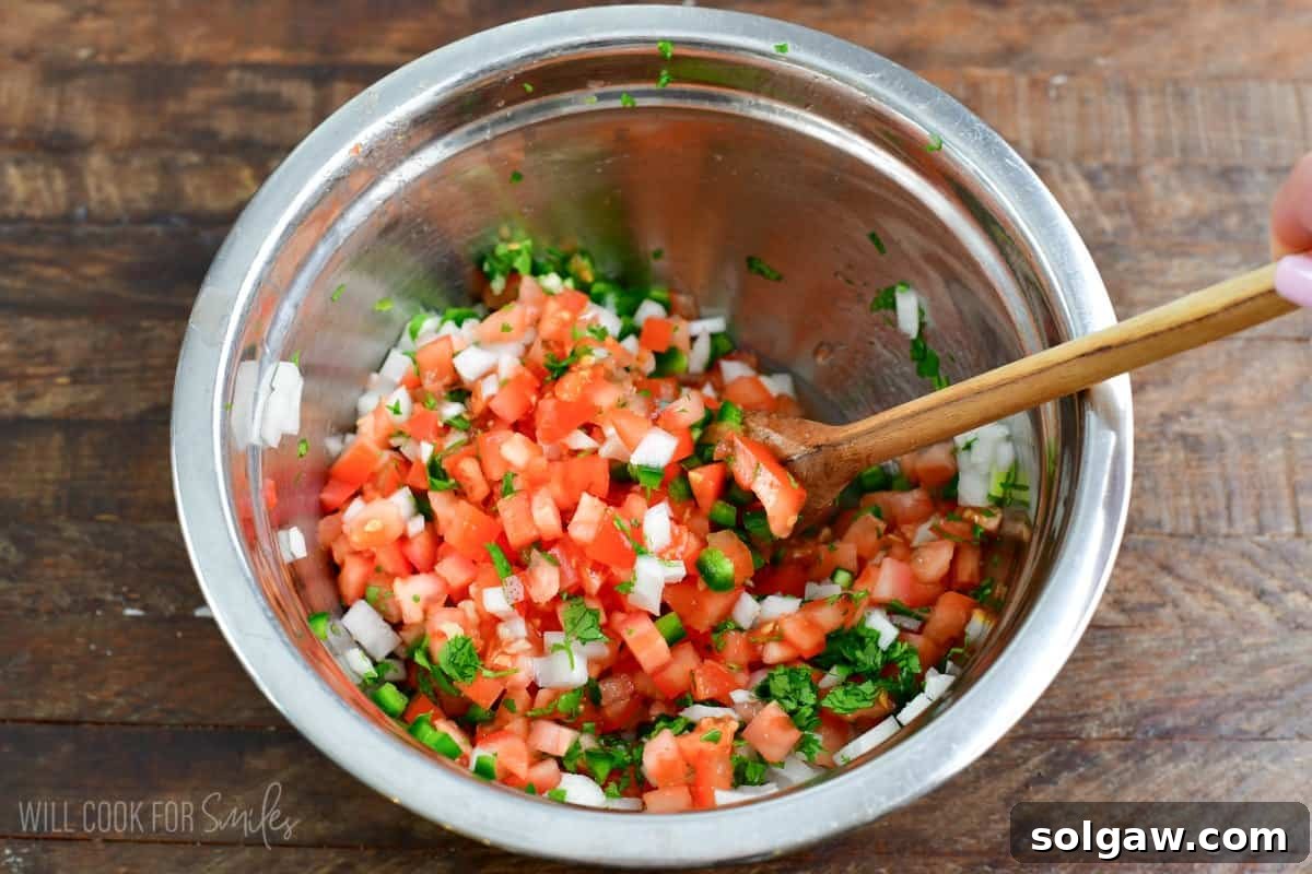 Gently stirring fresh Pico de Gallo in a glass bowl with a wooden spoon to combine all ingredients.