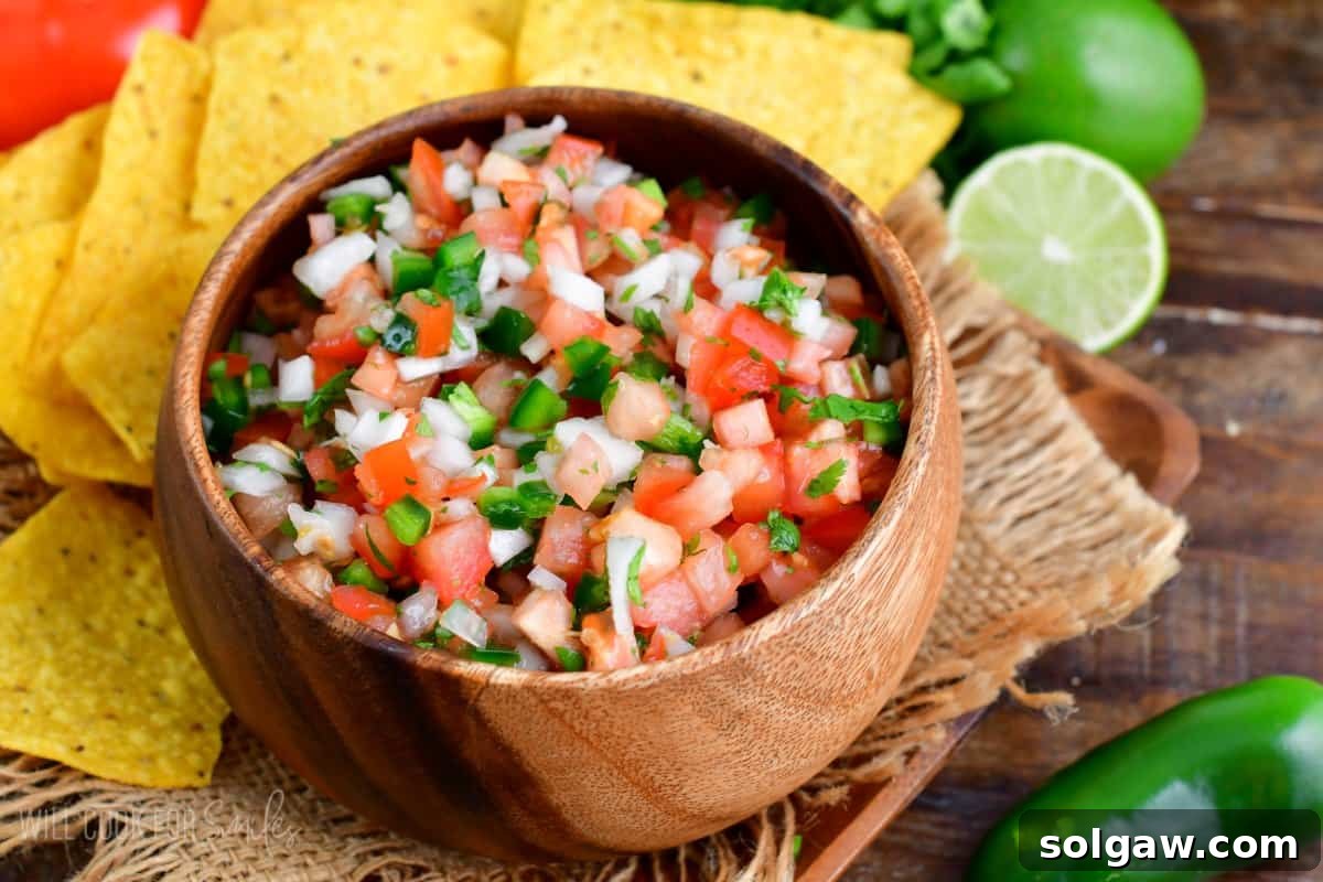 A beautifully presented bowl of Pico de Gallo, flanked by crispy tortilla chips, fresh lime wedges, and a whole jalapeño.