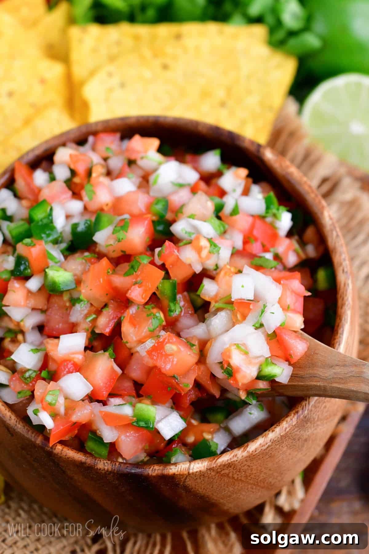 A wooden spoon poised to scoop a serving of vibrant Pico de Gallo from a rustic bowl, highlighting its fresh ingredients.
