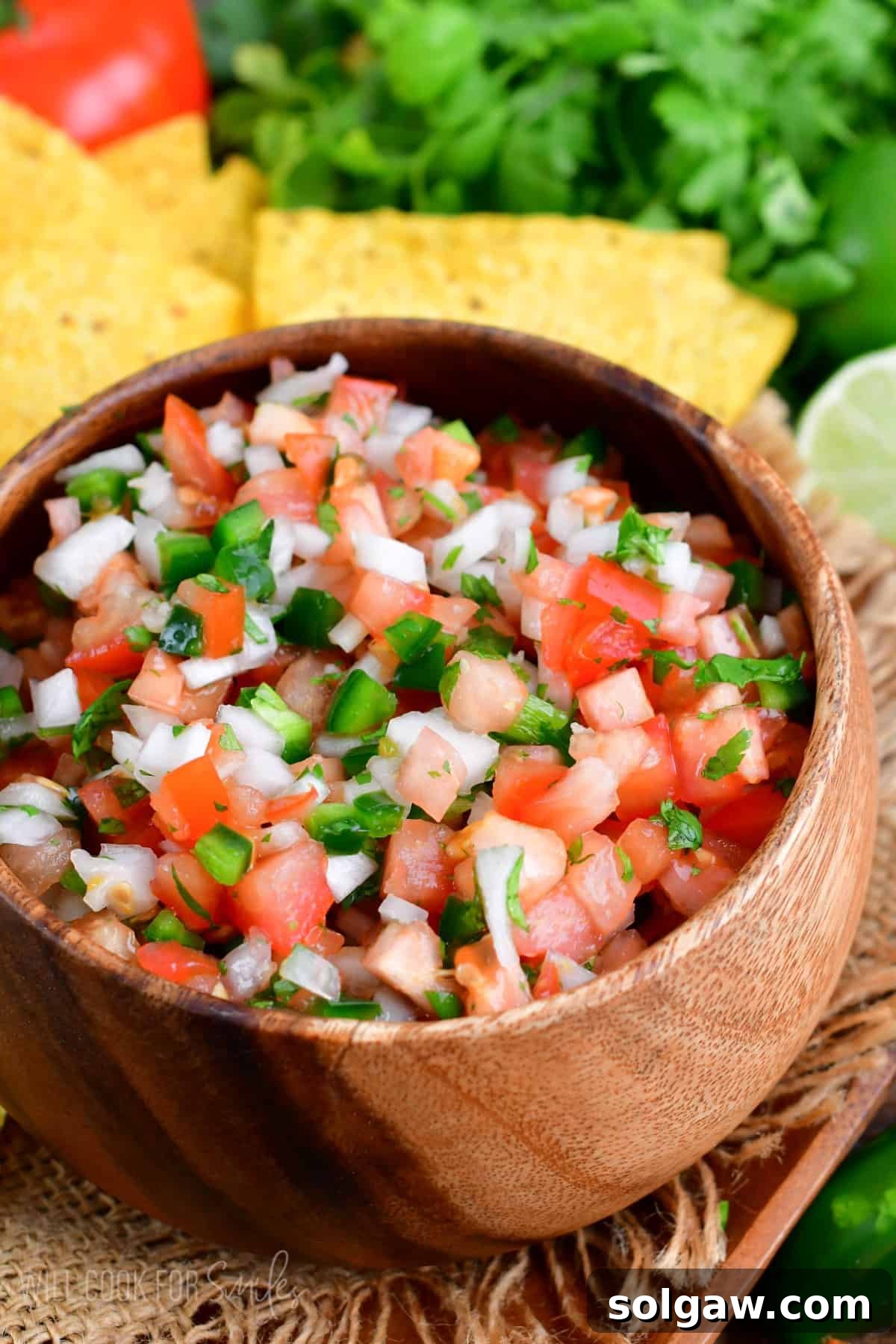 A close-up shot of vibrant Pico de Gallo in a wooden bowl set on a burlap placemat, ready to be enjoyed.