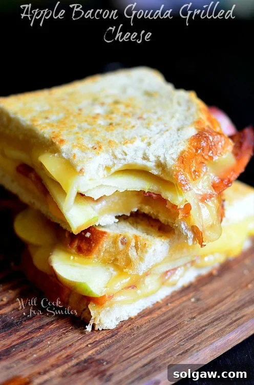A delicious Apple Bacon Gouda Grilled Cheese sandwich, with a bite taken out, showing the melted cheese, crisp bacon, and apple slices.