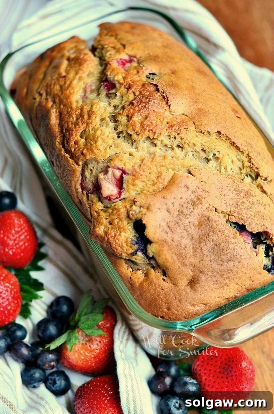 Berry bread in a glass bread pan with blueberries and strawberries on the bottom left