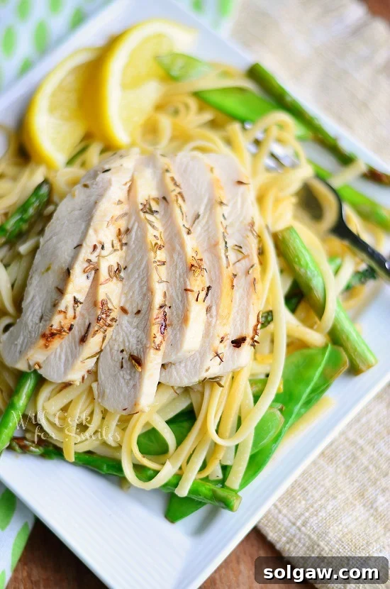 Linguine with Chicken, Asparagus and Snow Peas on a white square plate, garnished with lemon slices and served with a fork.