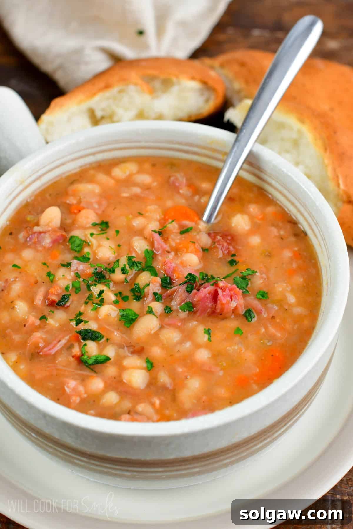 A hearty bowl of homemade ham and bean soup, garnished with fresh herbs, with a spoon nestled in the rich, creamy broth, ready to be enjoyed.
