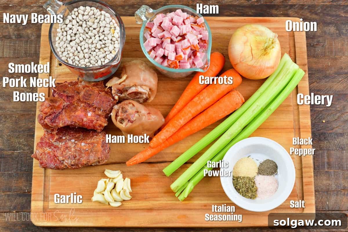An organized flat lay of key ingredients for ham and bean soup, featuring dried navy beans, smoked ham hock, fresh mirepoix (onions, carrots, celery), garlic, and a selection of herbs and spices.