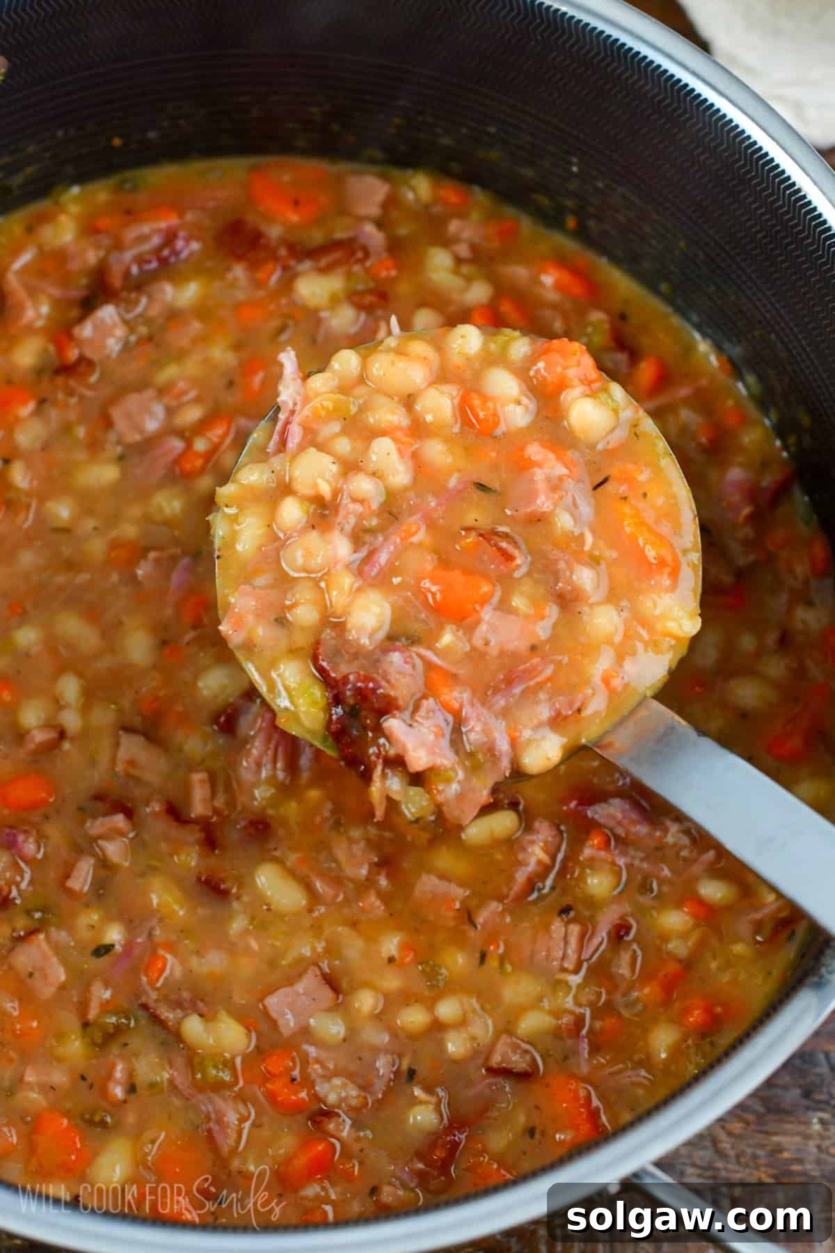 A ladle scooping a generous portion of steaming ham and bean soup from a large pot, highlighting its rich, creamy texture and hearty ingredients.