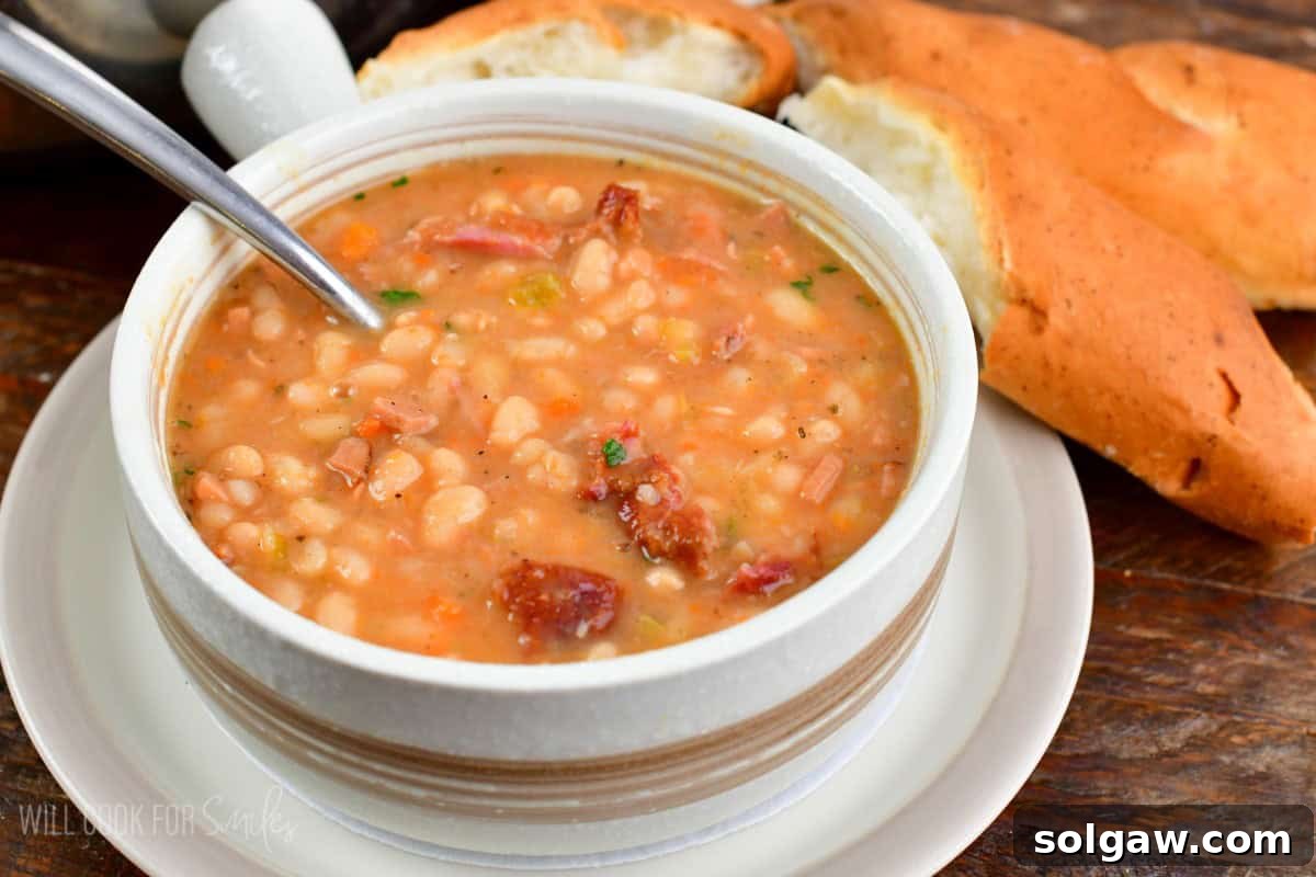 A beautifully presented bowl of ham and bean soup, ready to be enjoyed with a slice of rustic bread on the side, creating a classic comfort meal.