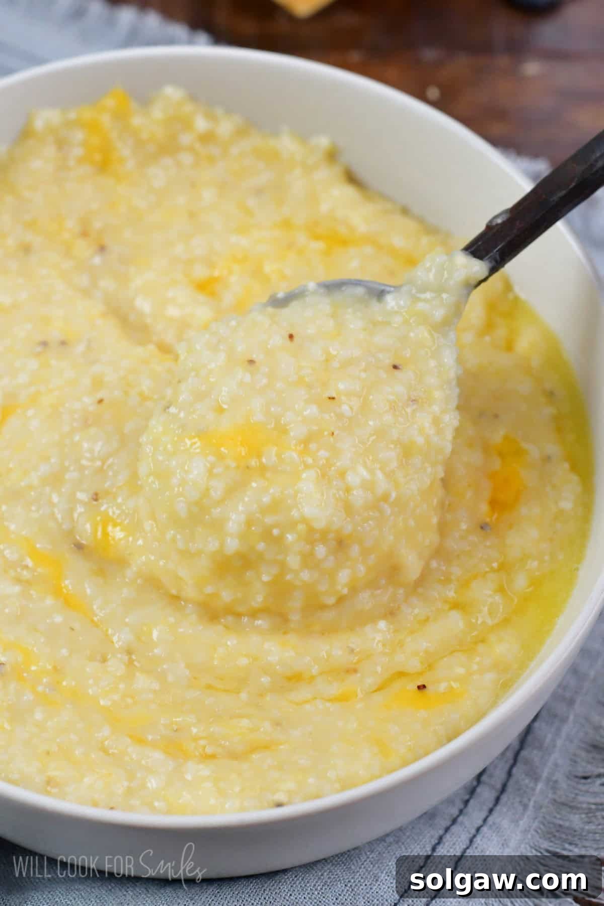 A spoon scooping creamy, golden cheese grits from a white bowl, showing its rich texture.
