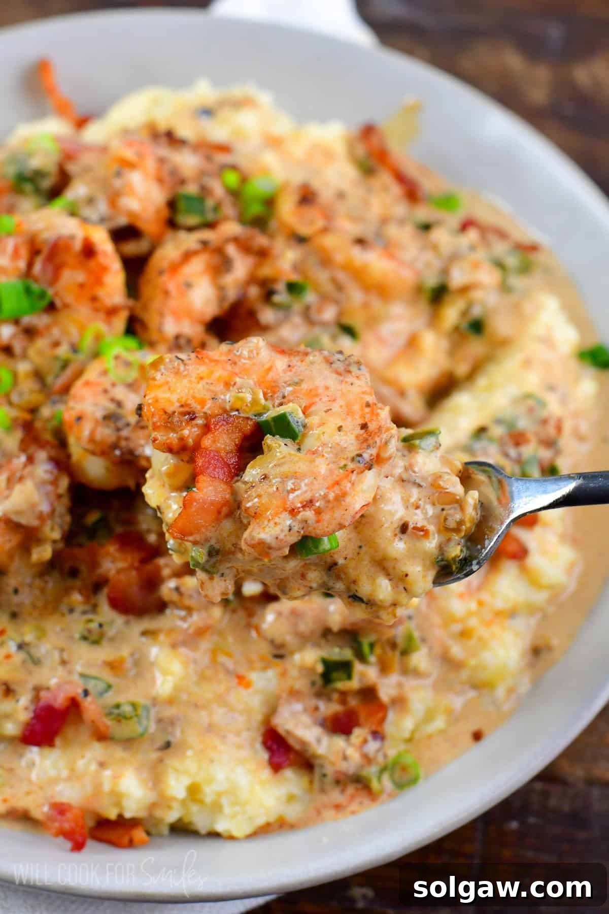 holding some creamy Cajun shrimp and grits on a fork over the bowl.
