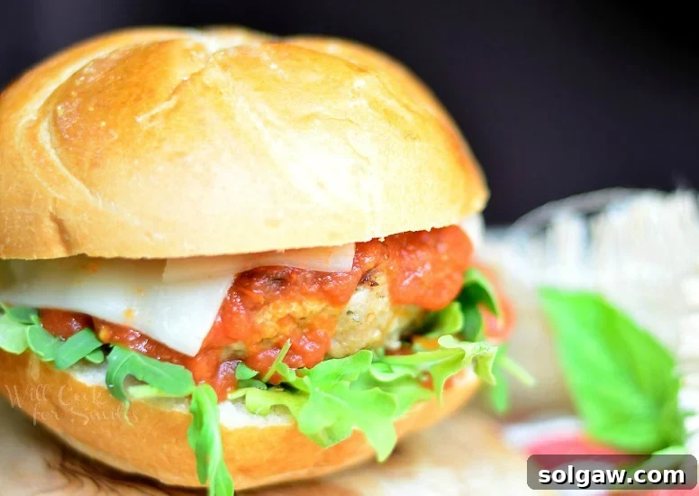 Horizontal photo of a Chicken Parmesan Burger with fresh basil on the bun, served on a wood cutting board, showcasing its melted cheese and juicy patty