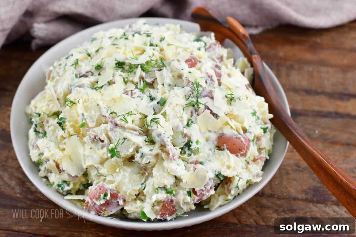creamy herb and parmesan potato salad in a gray bowl with a wooden spoon.