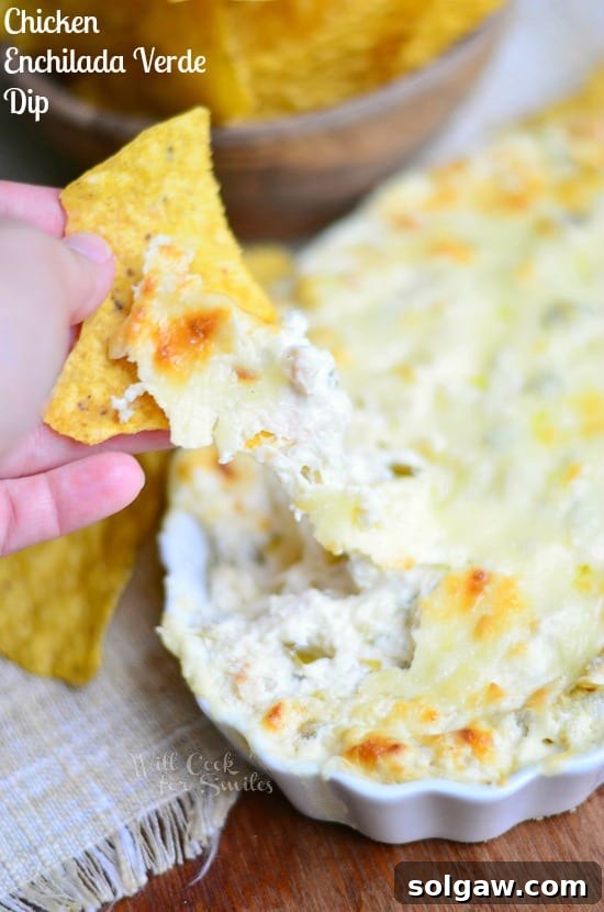 Dipping a chip into a warm, cheesy Chicken Enchilada Verde Dip in a white casserole dish
