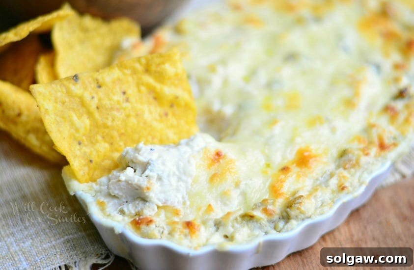 A chip being dipped into the Chicken Enchilada Verde Dip, showcasing the gooey cheese