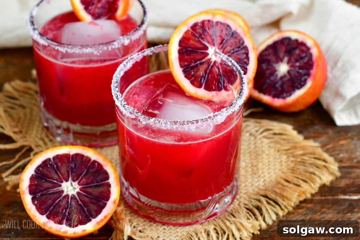 Two blood orange margaritas in a salt rimmed glass with a slice of blood orange as garnish.