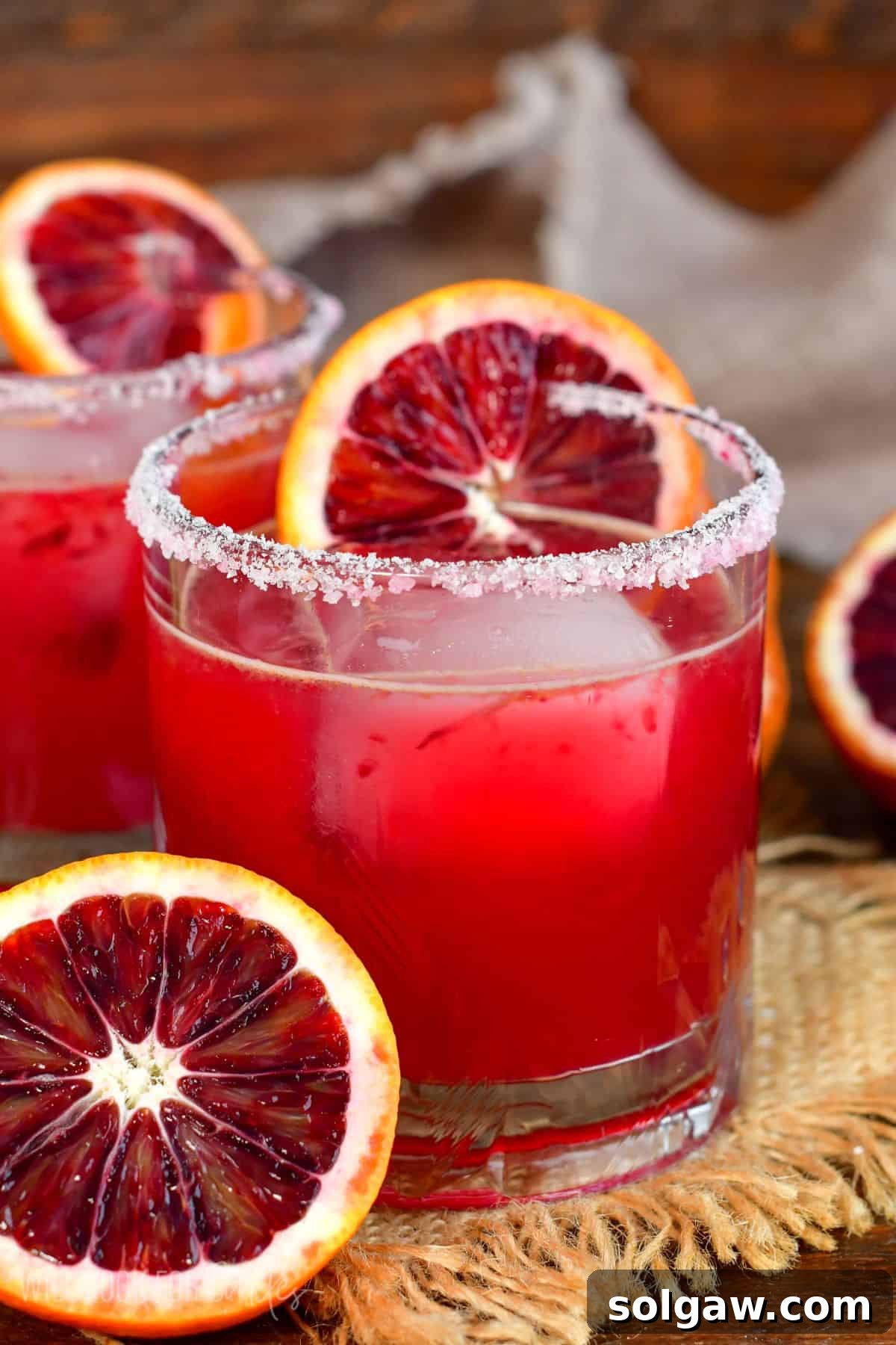Blod orange margarita in a salt rimmed glass with a slice of orange on the glass as garnish and half an orange next to the glass.