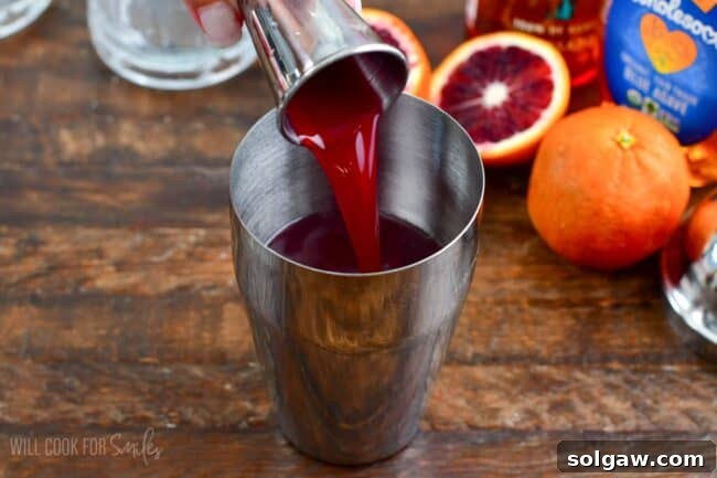 Pouring the blood orange juice into the metal shaker with oranges in the background.