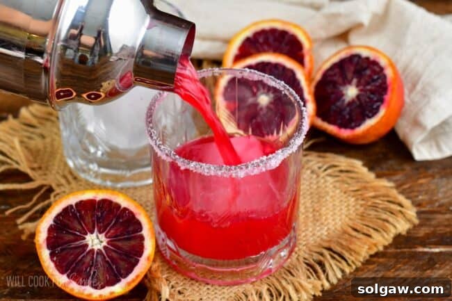 Pouring the blood orange margarita out of the shaker into a salt rimmed glass.