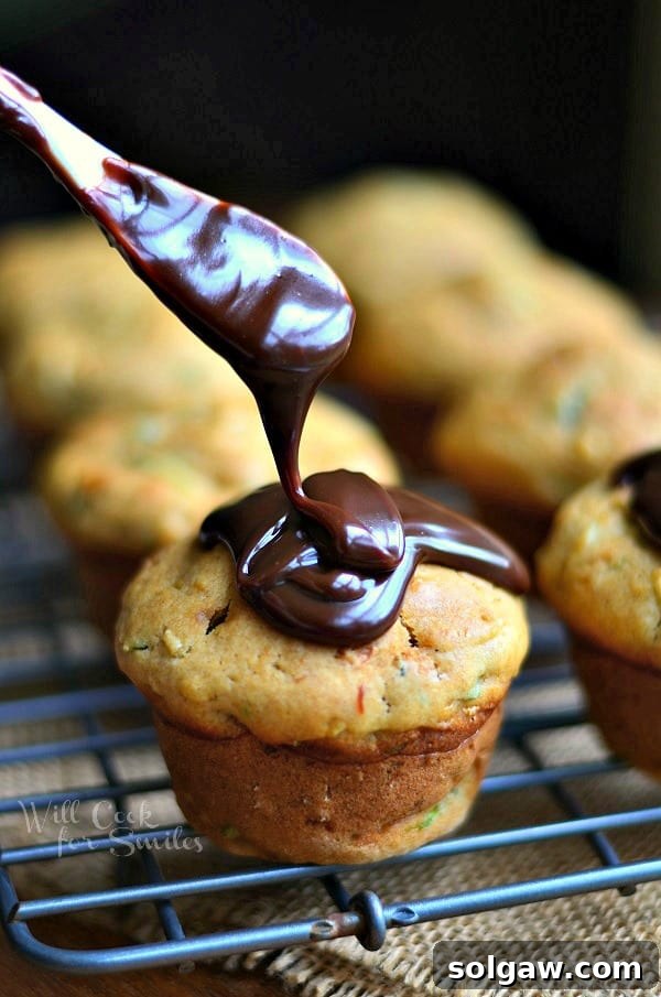 Rich Hot Fudge Sauce being generously poured over a Zucchini Muffin, with a small white spoon beside it.